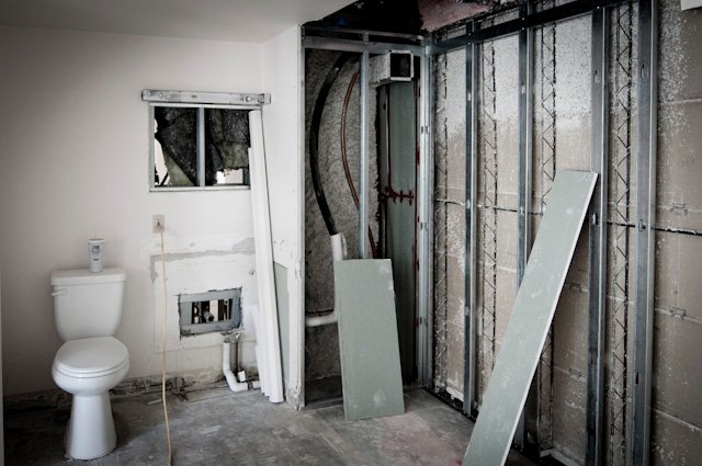 Bathroom under renovation with toilet, exposed wall framing, pipes, and unfinished shower area
