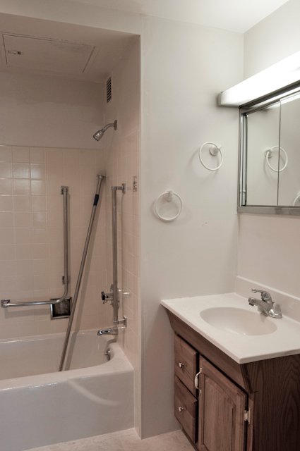 Bathroom with tiled tub and shower, white sink, wood vanity, and mirrored cabinet