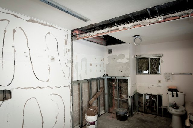 Partially demolished bathroom with exposed framing, plumbing, wiring, and toilet