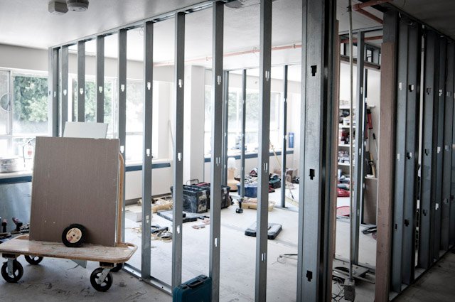 Interior renovation with exposed metal wall framing, drywall panels, and construction tools