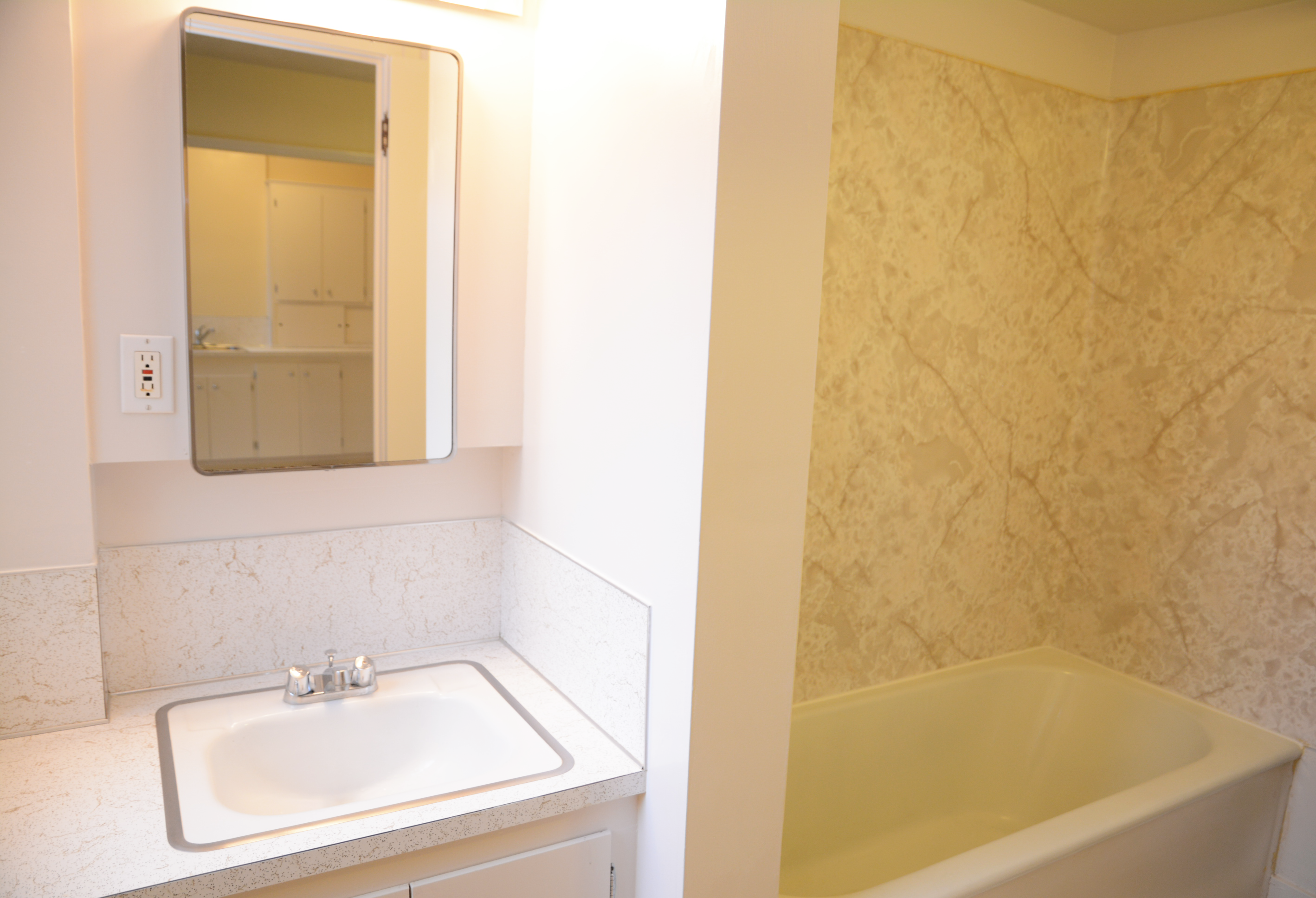 Bathroom with white sink, mirrored cabinet, and bathtub with beige marble-patterned surround