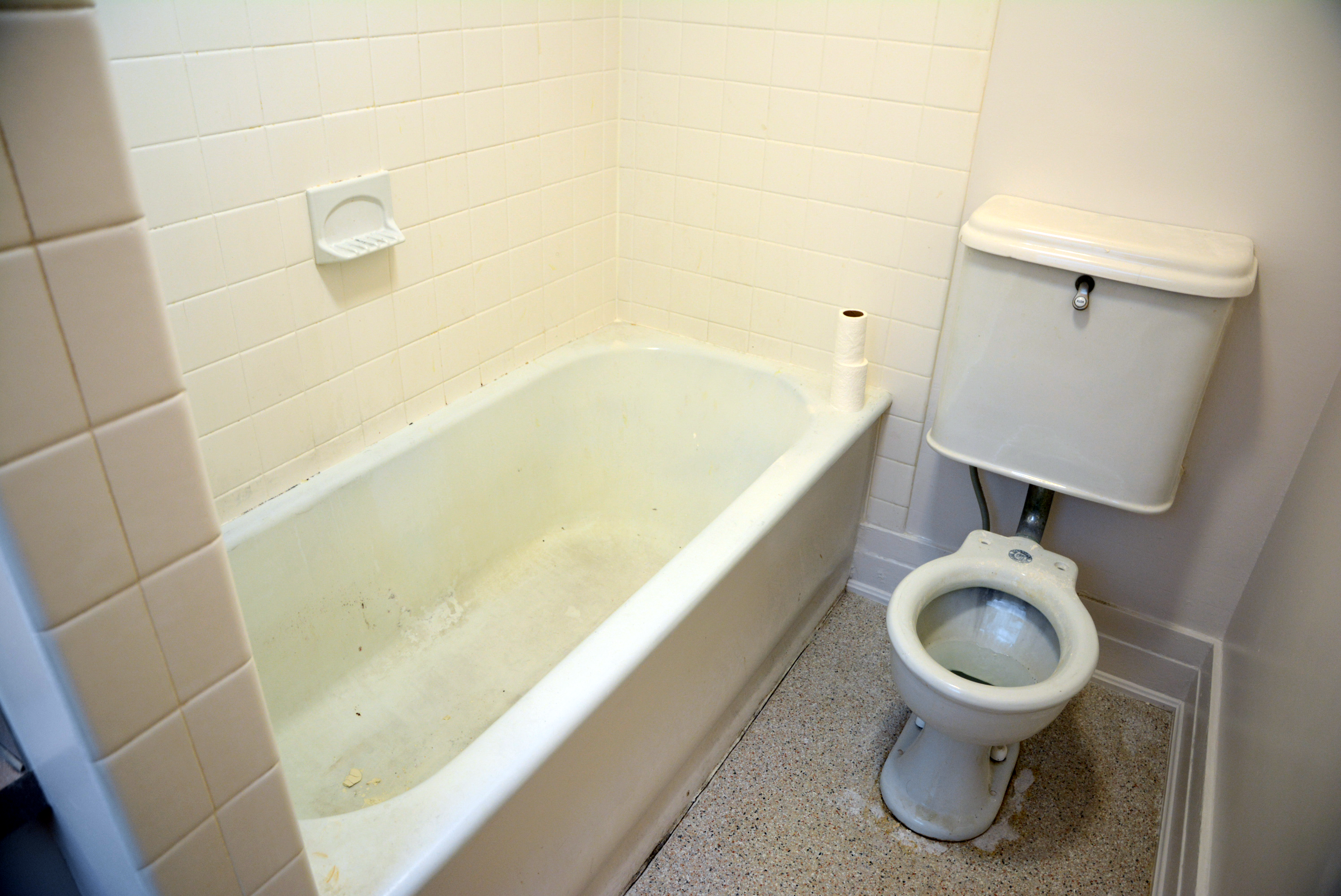Small bathroom with white tiled bathtub and toilet beside a speckled floor