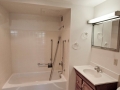 White bathroom with tiled tub and shower, wood vanity, sink, and mirrored cabinet