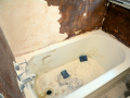 Bathtub under renovation with partially removed wall tile and exposed dark backing