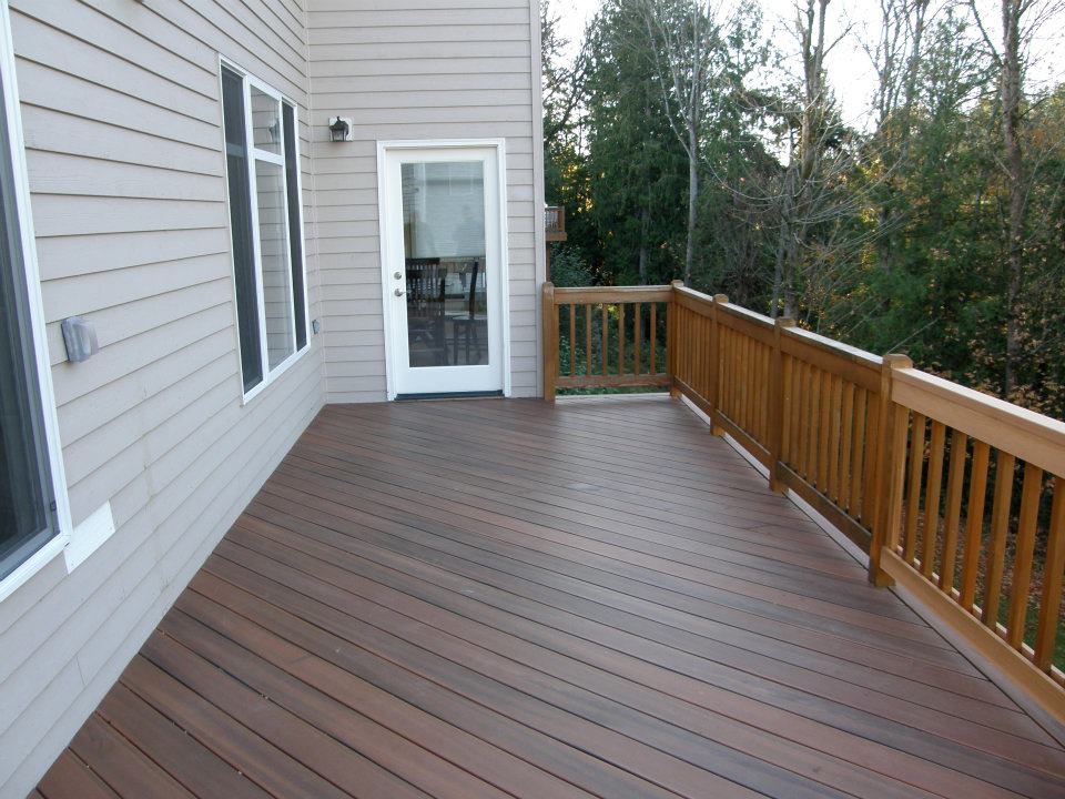 Large wooden deck with railing along the side of a gray house