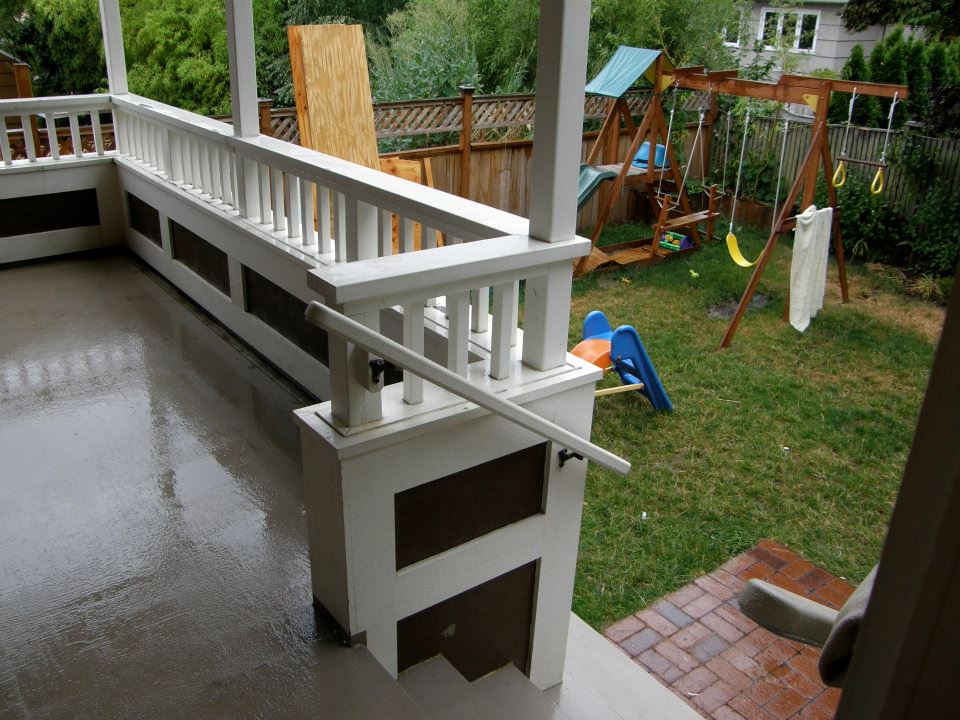 Covered porch with white railing and steps overlooking a backyard swing set