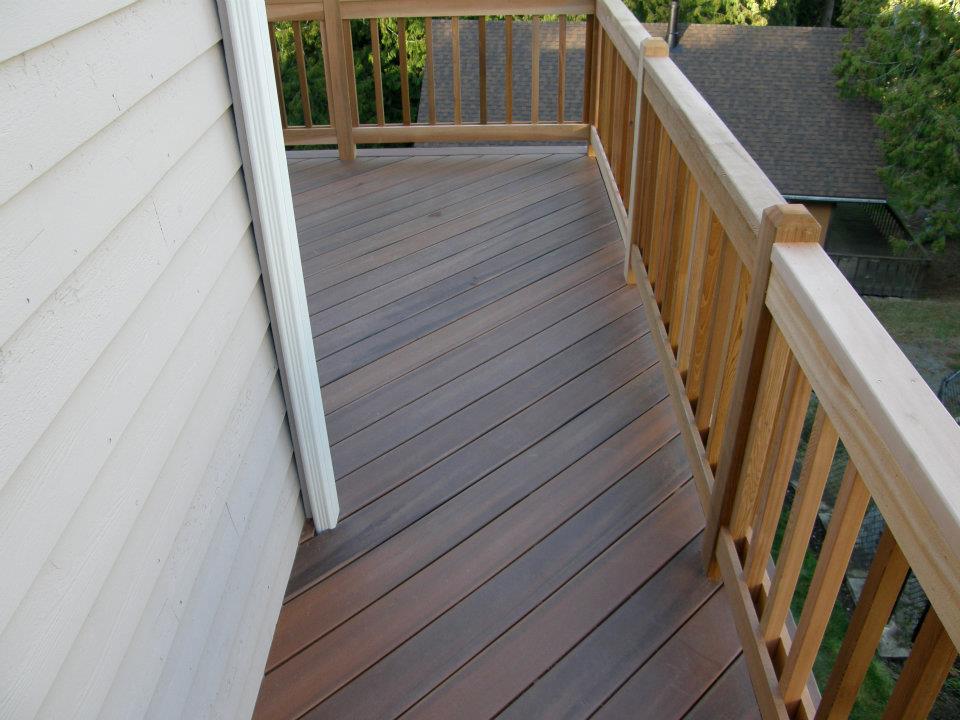 Narrow elevated deck with brown floorboards and natural wood railings beside a house