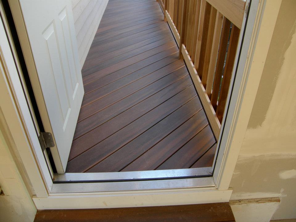 Open doorway leading to a narrow brown wood deck with natural wood railing