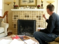 Man seated beside a beige tiled fireplace holding papers and gesturing