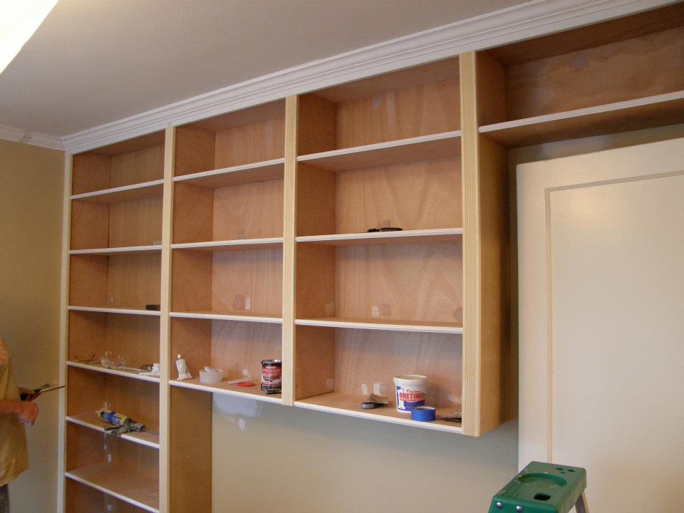 Built-in wood shelving under construction with open shelves and painting supplies