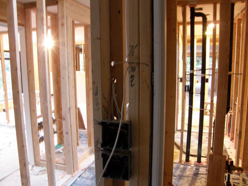Exposed wood wall framing with black plumbing pipes and electrical wiring