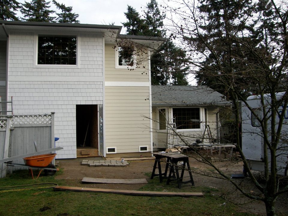 Two-story house exterior under renovation with scaffolding, tools, and an open doorway