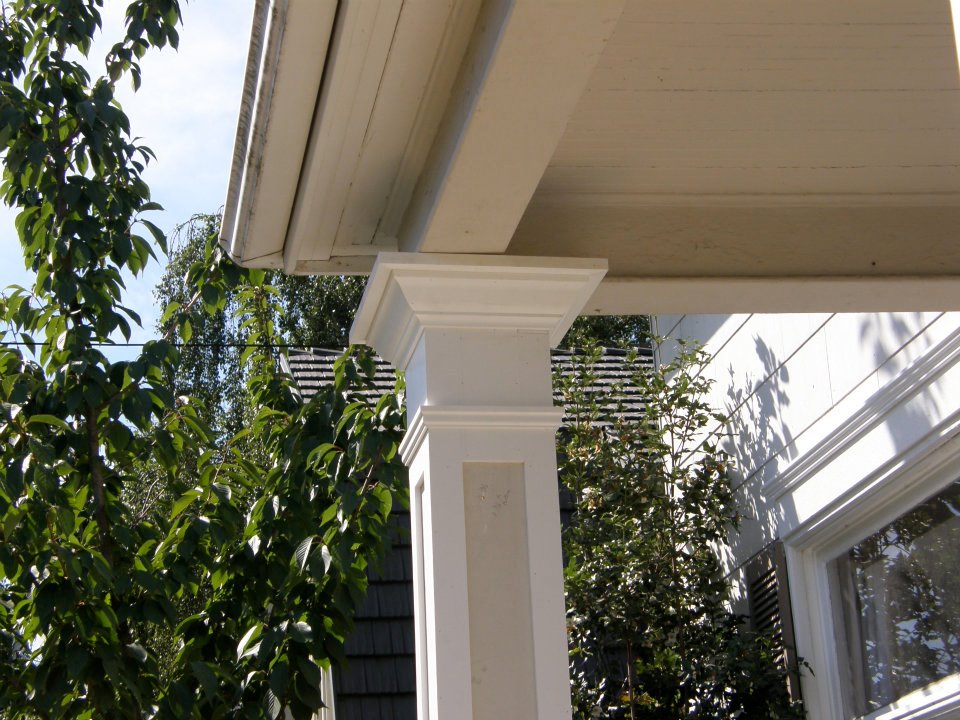 White decorative porch column supporting a roof overhang beside leafy trees