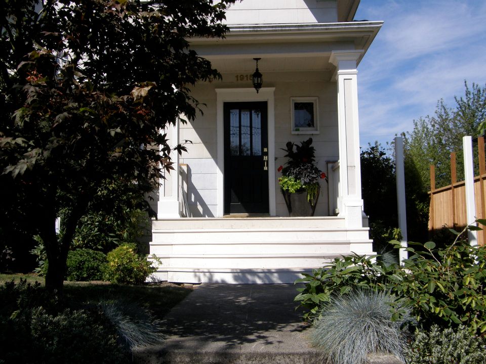 White front porch with black door, wide steps, decorative columns, and potted plants