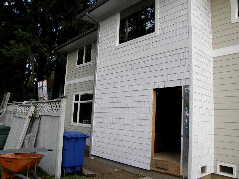Two-story house with white shingle siding and an unfinished doorway during renovation