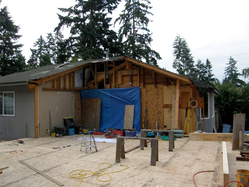 Home addition under construction with exposed roof framing, plywood walls, and tools