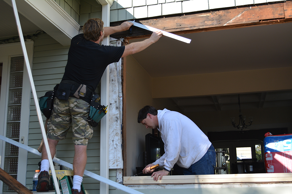 Two workers installing trim around a large opening on the front of a house