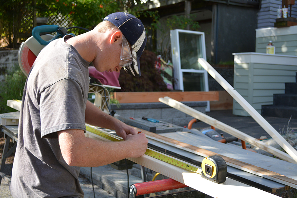 Worker wearing safety glasses measures and marks a long wooden board