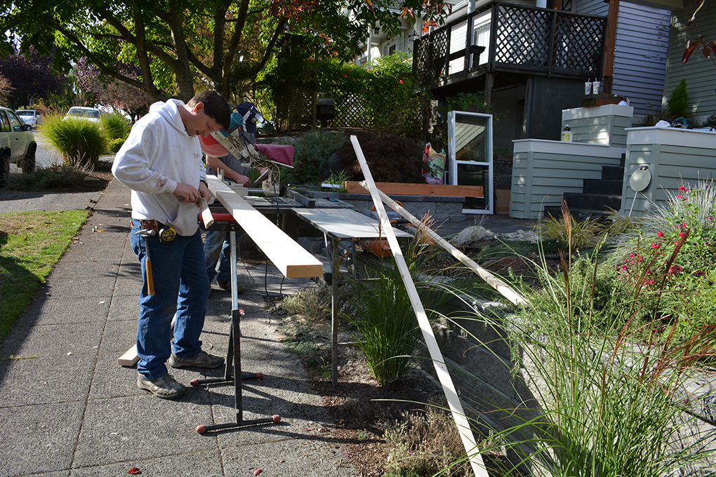 Construction worker measuring lumber beside a miter saw and outdoor work area