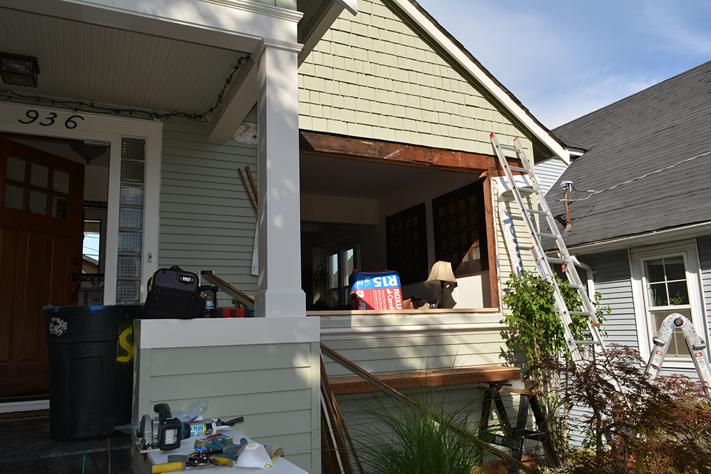 Front porch under renovation with a large wall opening, ladders, tools, and exposed wood