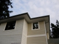 Upper exterior of a beige house with white trim, mixed siding, windows, and roof overhangs