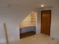 Unfinished room with built-in desk nook, wood shelves, brown door, and recessed lights