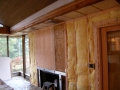 Exposed wall framing with yellow insulation surrounding a fireplace during renovation