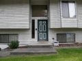White-sided home entrance with green door, concrete steps, and barred lower windows