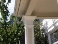 White decorative porch column supporting a roof overhang beside leafy trees