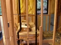 Exposed wall framing with black plumbing pipes, yellow insulation, and a window