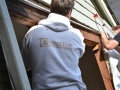 Two workers install white trim above an exposed wood-framed opening