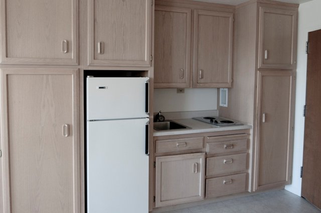 Compact kitchen with light wood cabinets, white refrigerator, sink, and two-burner cooktop