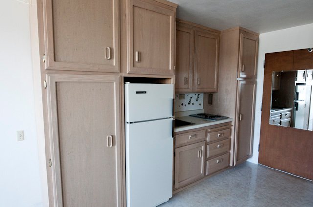 Compact kitchen with light wood cabinets, white refrigerator, sink, and cooktop