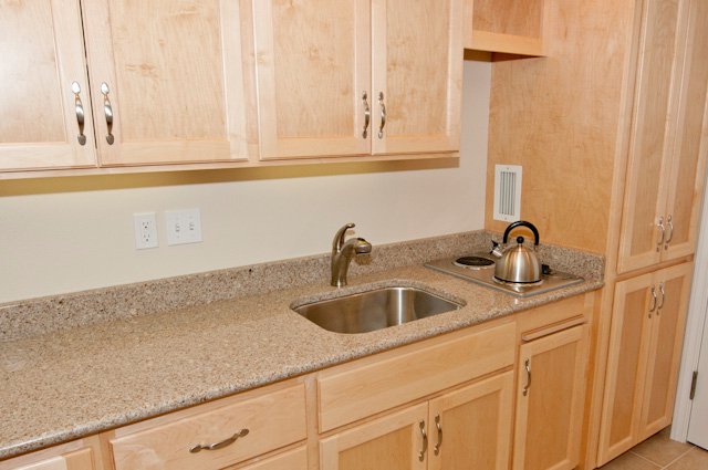 Light wood kitchen cabinets with granite countertop, sink, cooktop, and kettle