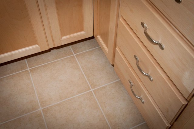 Light wood cabinet doors and drawers with silver handles above beige tile flooring