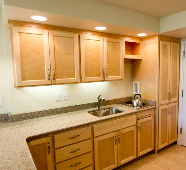 Light wood kitchen cabinets with granite countertop, sink, cooktop, and kettle