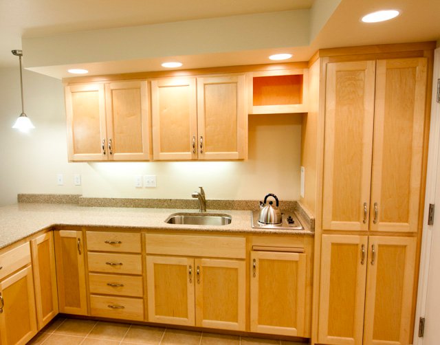 L-shaped kitchen with light wood cabinets, sink, cooktop, and speckled countertops