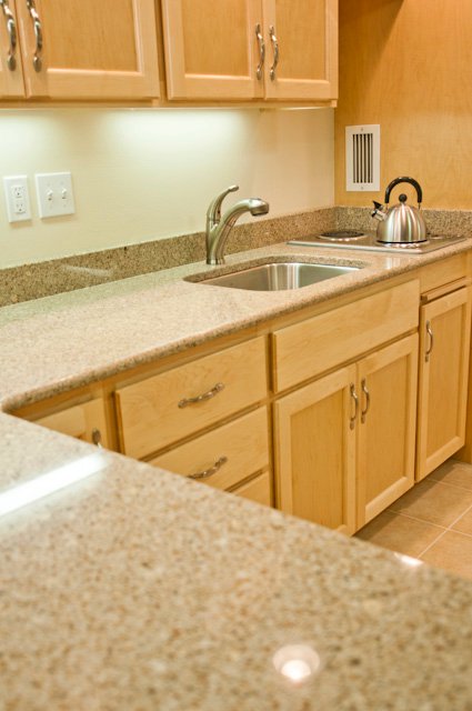 Light wood kitchen cabinets with speckled countertop, stainless steel sink, and kettle