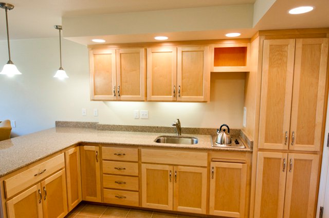 Light wood kitchen cabinets with L-shaped counter, sink, and stovetop