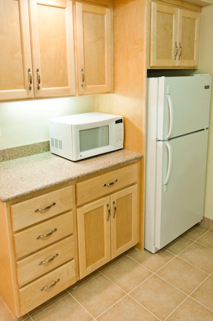 Light wood cabinets with microwave, refrigerator, and granite countertop