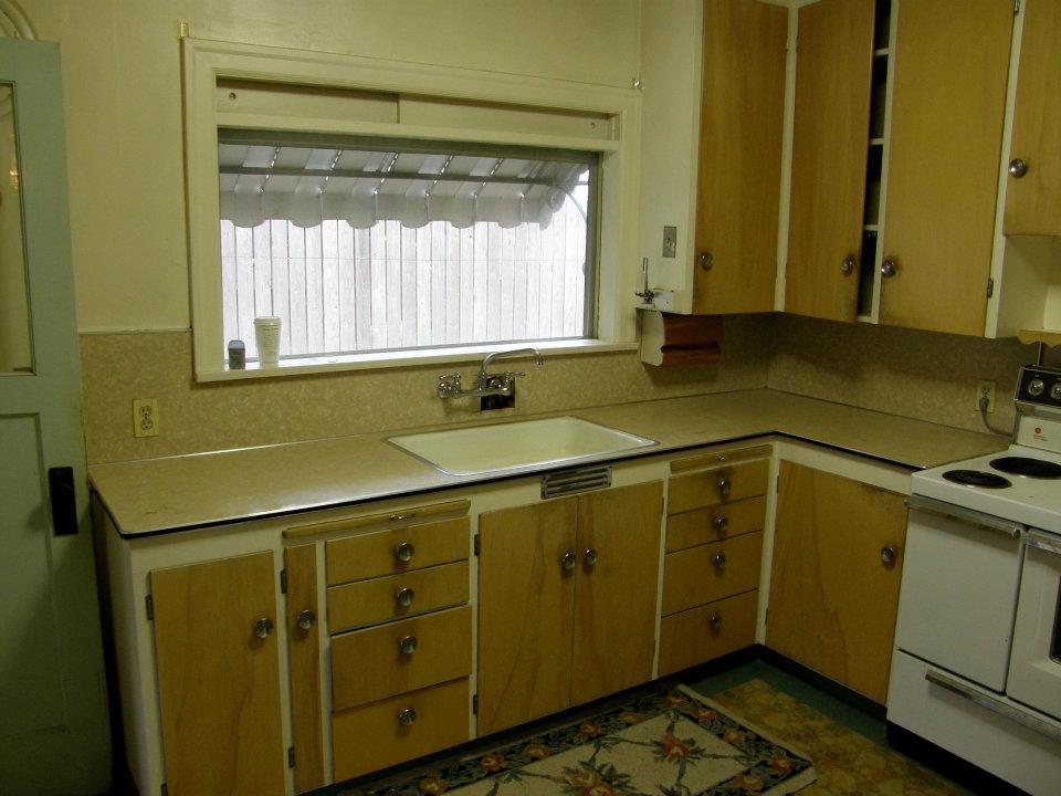 Older kitchen with wood cabinets, beige counters, sink, and white stove