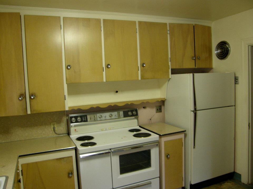 Older kitchen with light wood cabinets, white electric stove, and refrigerator