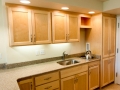 Light wood kitchen cabinets with granite countertop, sink, cooktop, and kettle