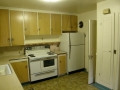 Older kitchen with wood cabinets, white electric stove, and refrigerator