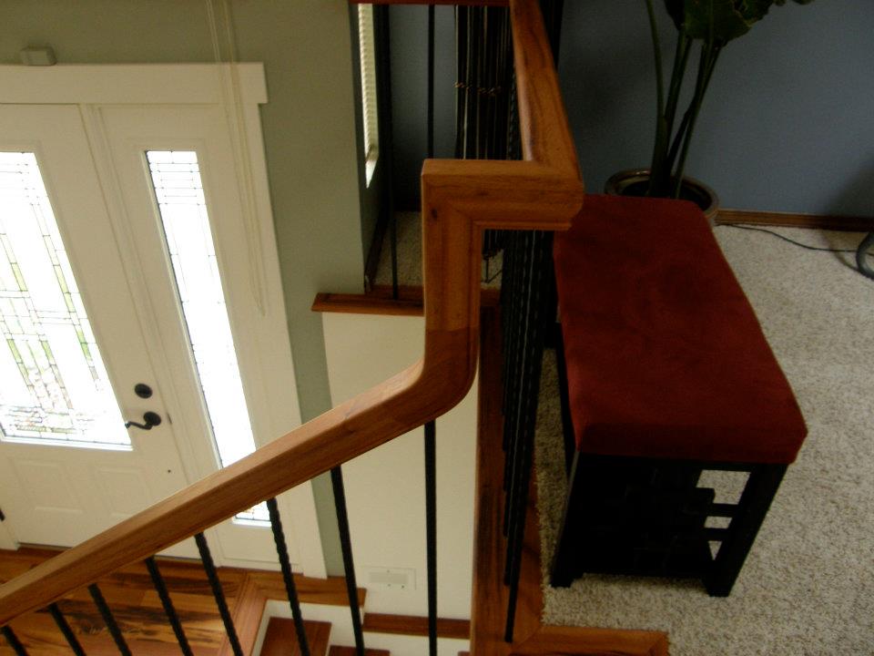 Wood stair railing with black balusters overlooking a white front door and entryway