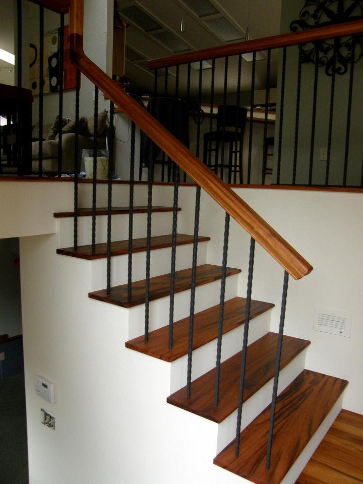 Wood staircase with white risers, black metal balusters, and matching wood handrail