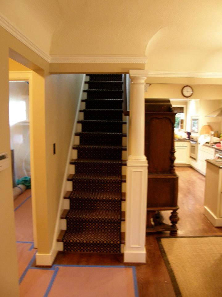 Carpeted staircase beside a white column leading upstairs from the kitchen