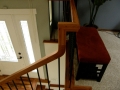 Wood stair railing with black balusters overlooking a white front door and entryway