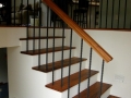 Wood staircase with white risers, black metal balusters, and matching wood handrail