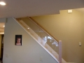 Carpeted staircase with a glass railing and wood handrail against a beige wall